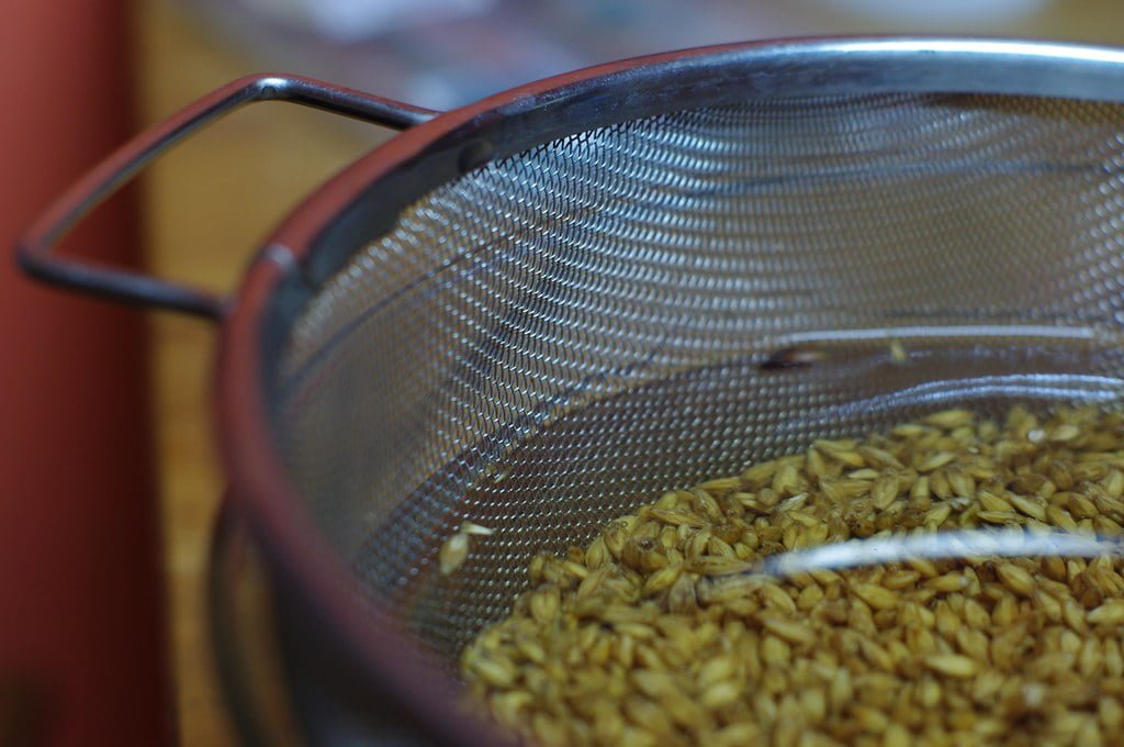 A close-up of uncooked grains in a metal mesh strainer.