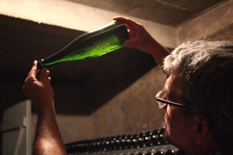 A man examining a bottle of wine by holding it up to the light in a dimly lit room.