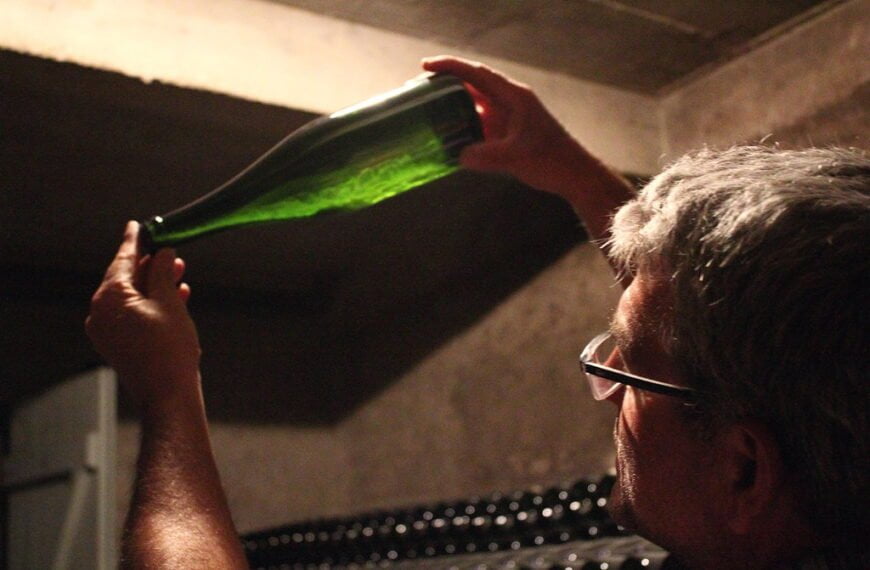 A man examining a bottle of wine by holding it up to the light in a dimly lit room.