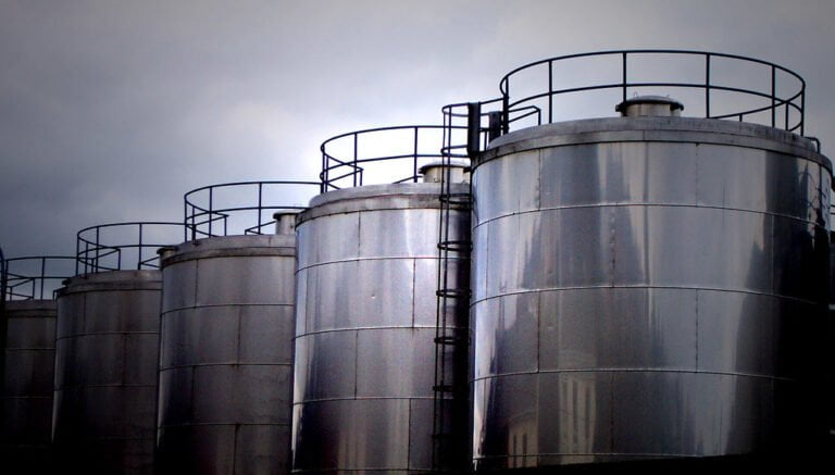Several large industrial storage tanks with reflective metal surfaces against a cloudy sky.