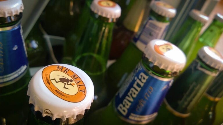 A close-up view of various beer bottles with focus on a cap labeled "MR. MALT" in the foreground, surrounded by other bottles with green glass and labeled caps, including one that reads "Bavaria."