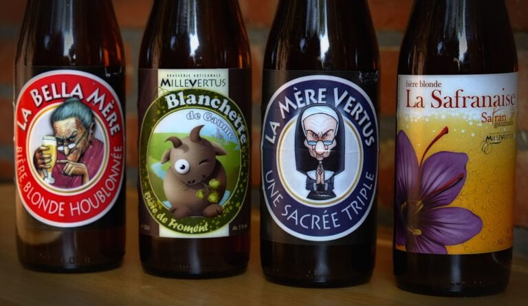 Four bottles of beer with illustrated labels displayed side by side. From left to right, the labels feature a cartoon of an elderly woman drinking beer, a smiling pig holding hops, an angry elderly nun, and a large purple flower, respectively. Each label also contains text in French describing the beer type and brand.