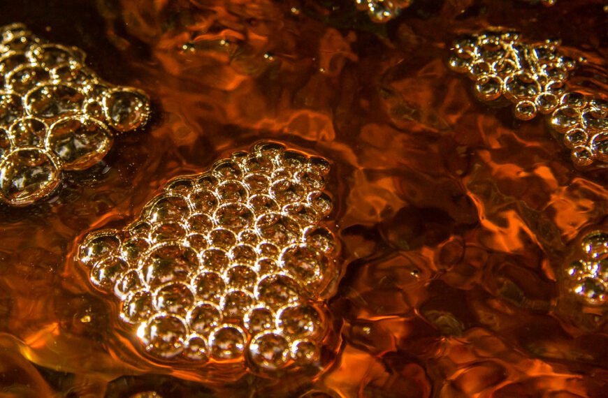 Close-up of transparent bubbles on a shimmering amber-colored liquid surface.