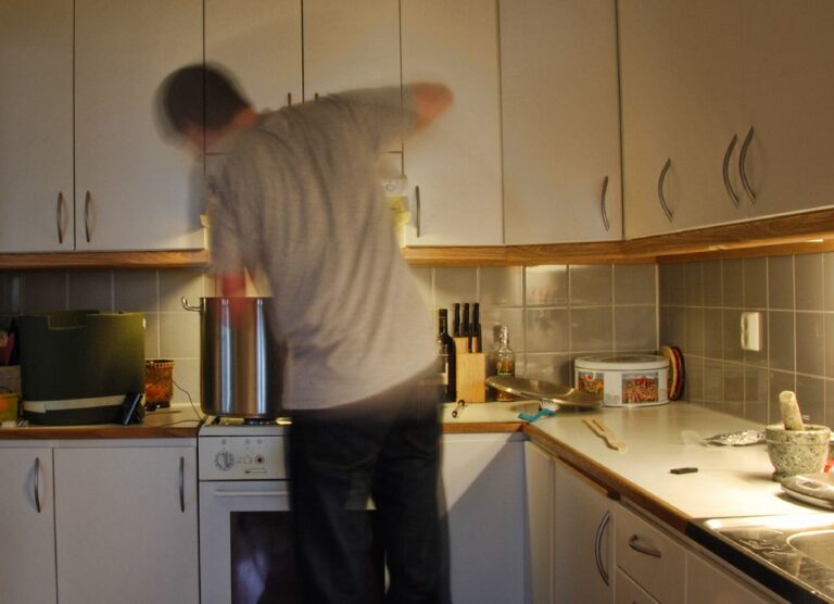 A motion-blurred person cooking in a modern kitchen with wooden cabinets and various kitchen utensils on the counter.