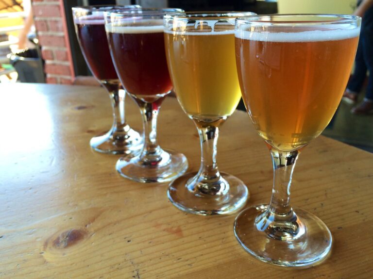 A flight of beer in tasting glasses with varying colors from dark brown to light golden arranged on a wooden table.