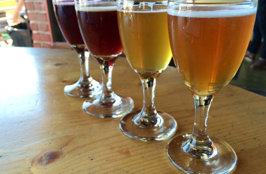 A flight of beer in tasting glasses with varying colors from dark brown to light golden arranged on a wooden table.