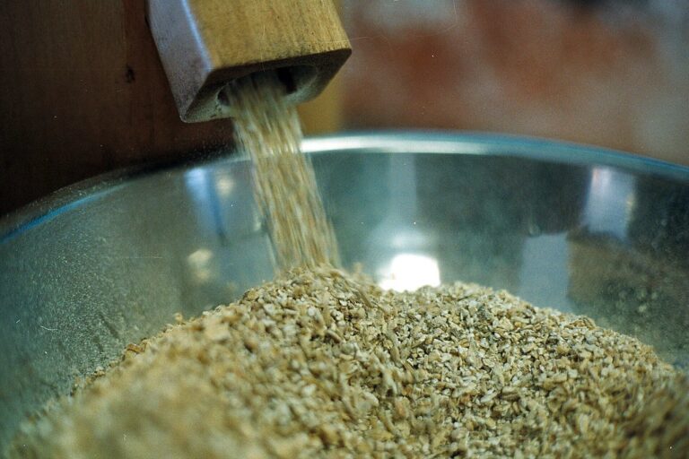 Whole grains being poured from a wooden chute into a stainless steel bowl.