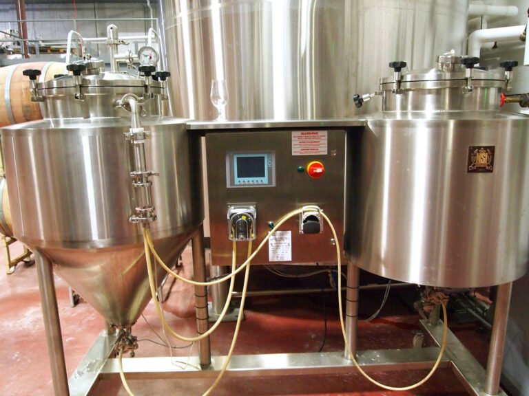 Stainless steel brewery equipment with gauges, pipes, and electronic control panel, located indoors.