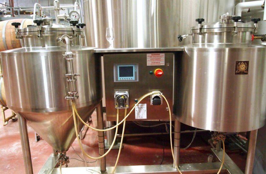 Stainless steel brewery equipment with gauges, pipes, and electronic control panel, located indoors.