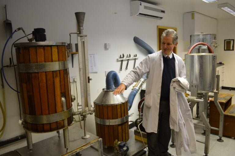 A person in a lab coat standing next to industrial fermentation equipment.