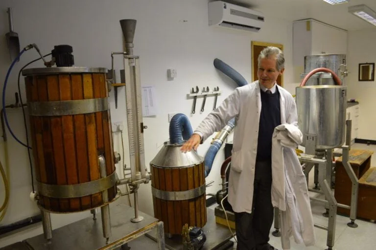 A person in a lab coat standing next to industrial fermentation equipment.