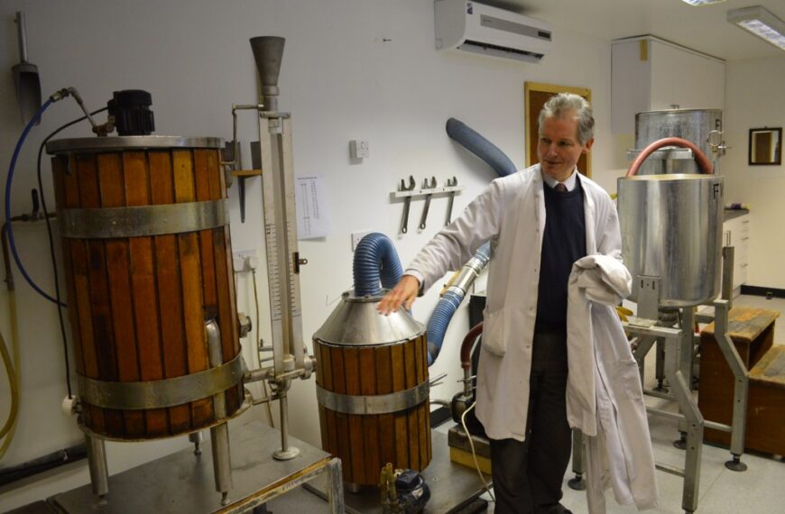 A person in a lab coat standing next to industrial fermentation equipment.