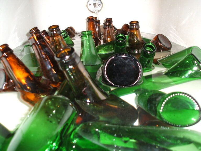 A collection of empty glass bottles in green and brown scattered haphazardly, some upright and others lying on their sides, with reflections visible on a shiny surface.