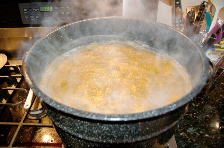 A pot with boiling contents emitting steam on a stove, with a digital clock displaying 12:33 in the background on a microwave.