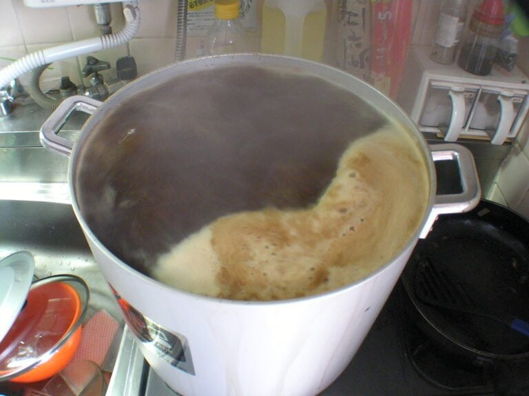 A large pot overflowing with foam on a stove next to a sink full of dishes.