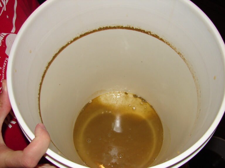 A white plastic bucket held by a person, showing a brown residue and a small amount of dirty liquid at the bottom.