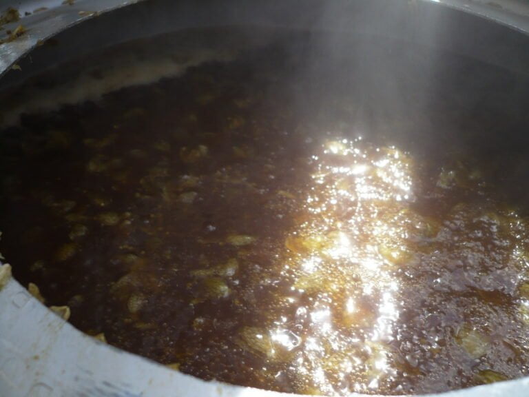 A pot of simmering liquid with steam rising above it, reflecting light, and some solid particles visible on the surface.