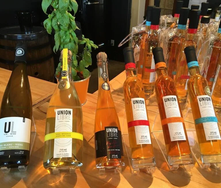 Several bottles of UNION LIBRE wine and cider are displayed on a wooden table, with a potted basil plant in the background.