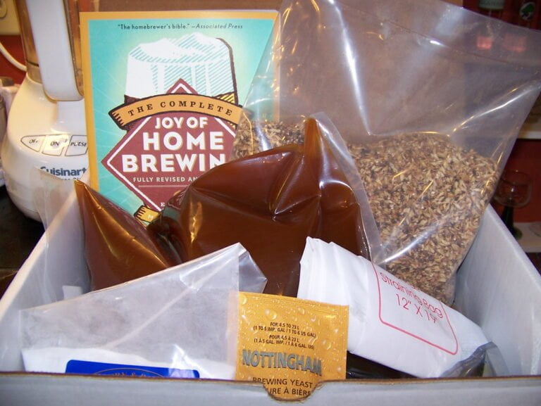 A homebrewing kit with various supplies including a book titled "The Complete Joy of Home Brewing," packets of yeast, and bags of grains.