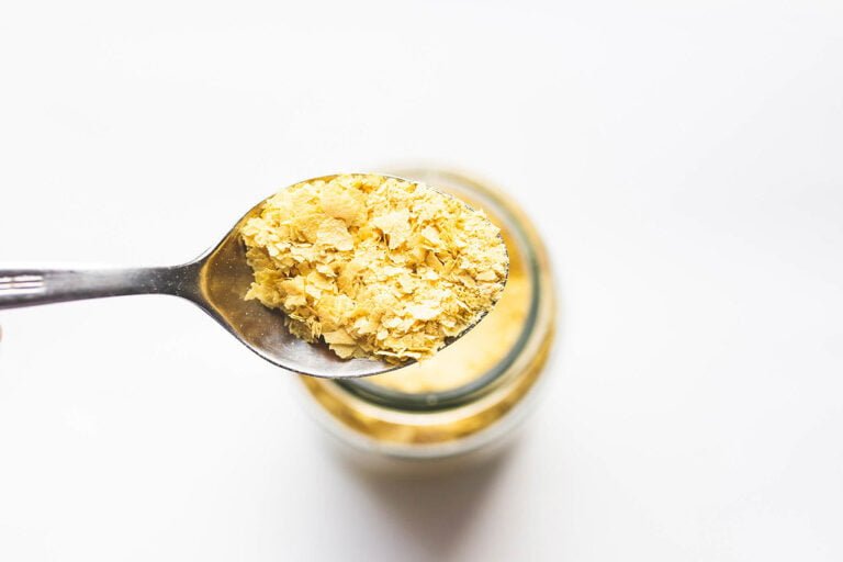 A spoonful of golden flaky nutritional yeast above a jar against a white background.
