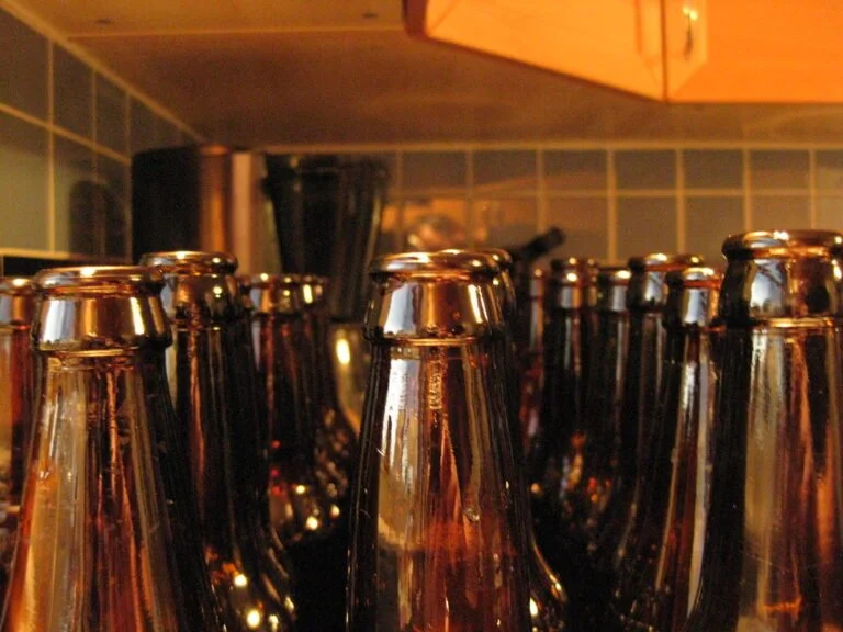 An array of empty brown glass bottles with a focus on their necks and openings, set against a softly lit kitchen backdrop.