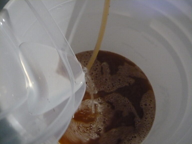 Liquid being poured into a white bucket creating a frothy surface.