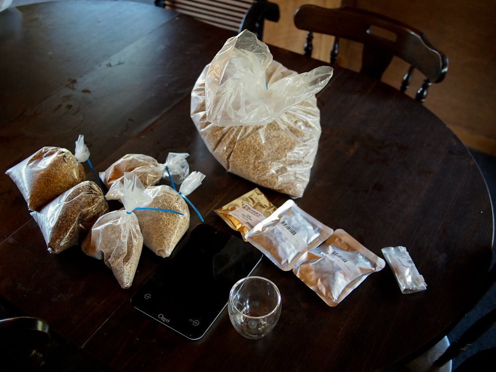 Various packets and bags of grains and seeds on a wooden circular table, with a digital scale and an empty glass cup.