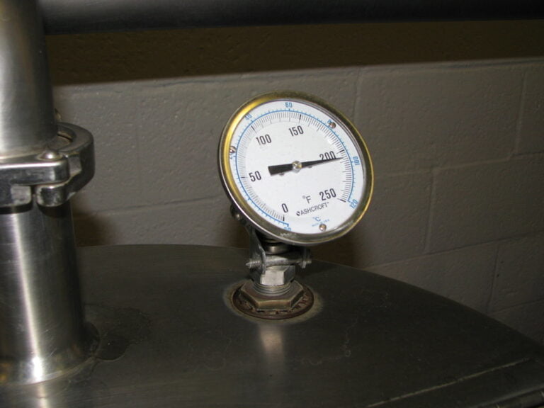 An analog pressure gauge with dual scale for psi and degrees Fahrenheit, mounted on an industrial pipe.