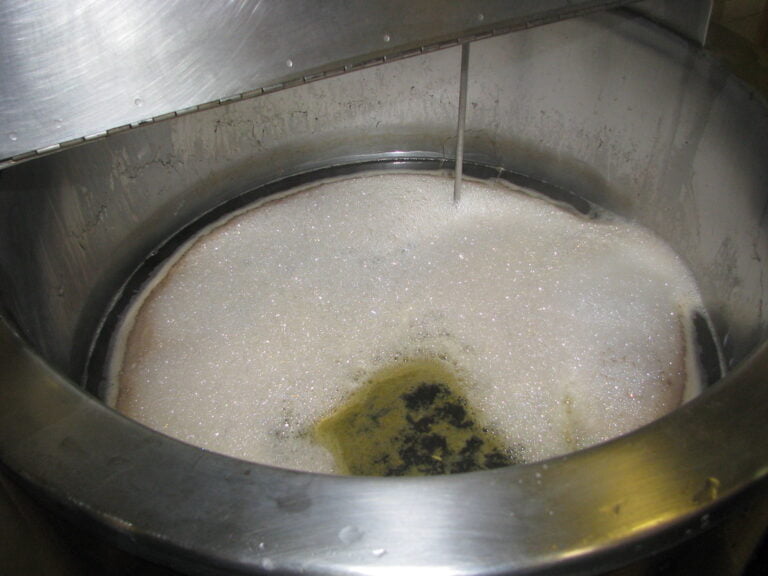 A large metal brewing kettle filled with foamy liquid during the beer brewing process.