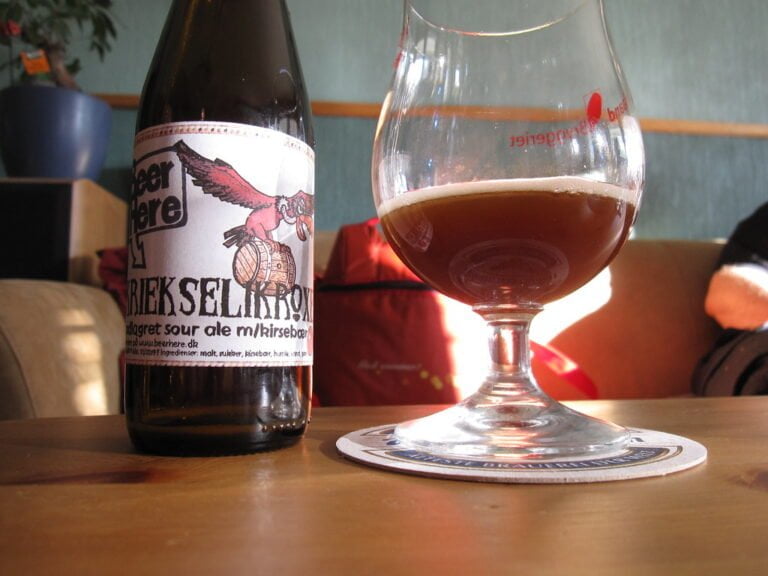 A bottle of KRIEK SELIKRON beer next to a glass of dark ale on a coaster, with the label featuring an illustration of a bird on a barrel.