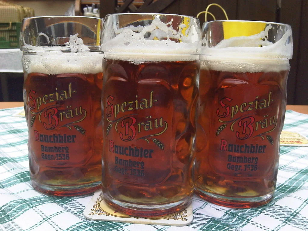 Three glasses of amber-colored beer with the label "Spezial Bräu Rauchbier Bamberg Gegr. 1536" on a checkered tablecloth.