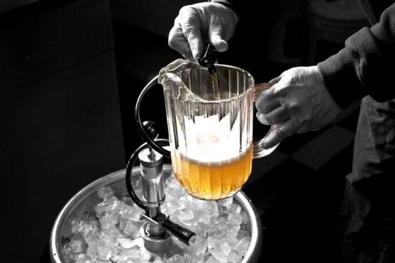 A black and white photo with a splash of color where a person's hands are pouring a golden beer from a tap into a clear pitcher, which is placed over a bucket filled with ice.