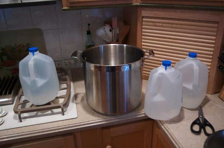 A kitchen counter with two empty plastic milk jugs and a large stainless steel pot on a stove top, with kitchen utensils in the background.