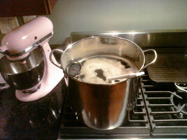 A large pot with boiling contents and a thermometer clipped to its side sits on a stove next to a pink stand mixer.