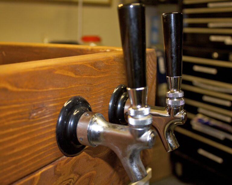 Two beer tap handles mounted on a wooden bar with a blurry background featuring workshop tools.