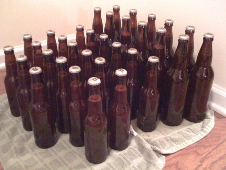 A collection of capped brown beer bottles arranged on a towel on the floor.
