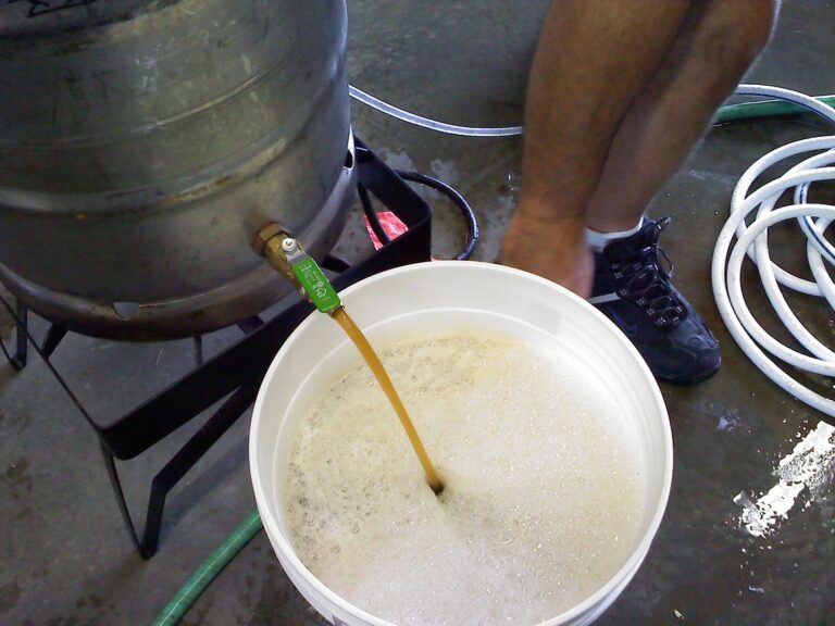 A person brewing beer with equipment, showing a liquid pouring from a beer keg into a white bucket full of foam, with various hoses on the ground.
