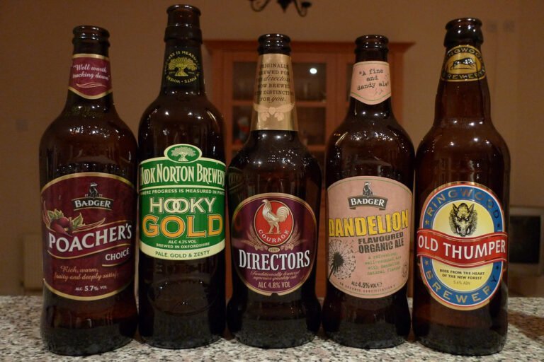 Five different bottles of British ales with labeled brands such as Badger, Hook Norton Brewery, and Ringwood Brewery, displayed in a row on a countertop.