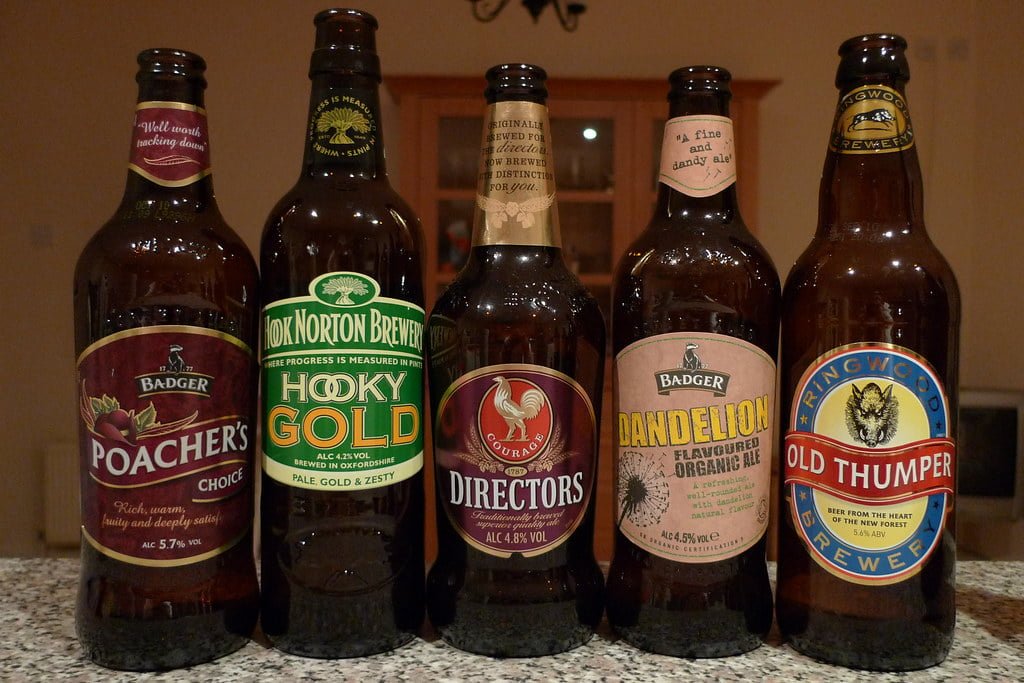 Five different bottles of British ales with labeled brands such as Badger, Hook Norton Brewery, and Ringwood Brewery, displayed in a row on a countertop.