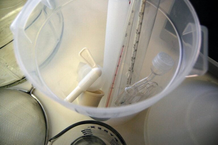 A view inside a plastic graduated cylinder with a pipette and a stirring rod, beside laboratory equipment including a beaker and sieve.
