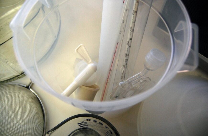 A view inside a plastic graduated cylinder with a pipette and a stirring rod, beside laboratory equipment including a beaker and sieve.