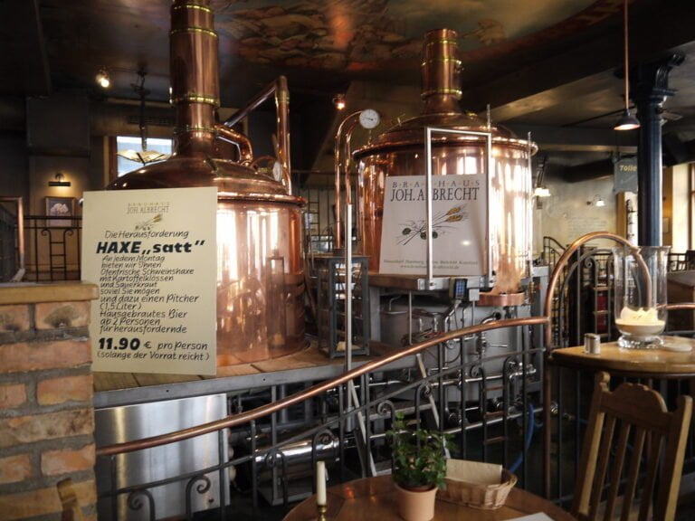 Interior of a brewery with copper brewing kettles, signage in German, and a rustic atmosphere.