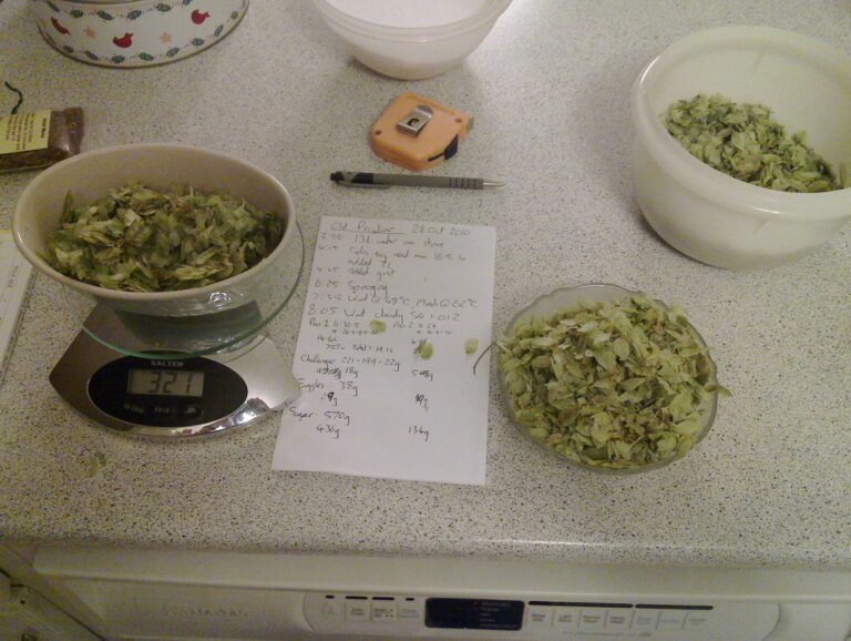 A kitchen countertop with chopped green leaves in a bowl on a digital kitchen scale showing 321 grams, another bowl with more leaves, a notepad with handwritten notes, a pen, and a utility knife.