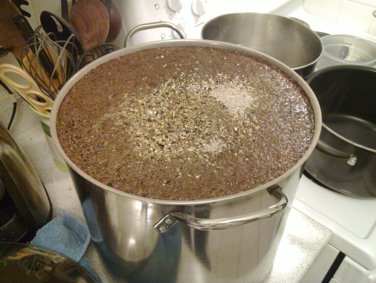 A large stainless steel pot on a kitchen stove filled with a substance topped with herbs, possibly in the process of cooking or brewing.