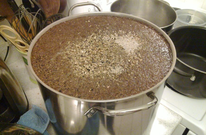 A large stainless steel pot on a kitchen stove filled with a substance topped with herbs, possibly in the process of cooking or brewing.