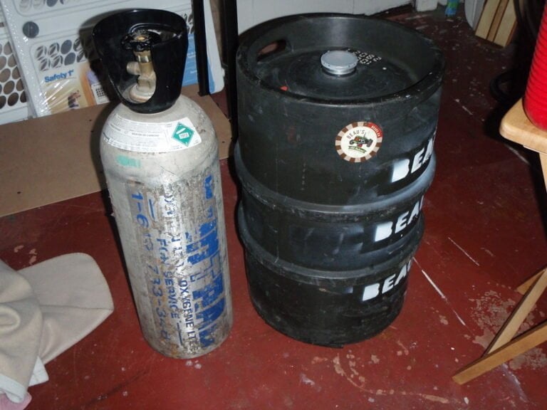 A used gas cylinder and a dark-colored beer keg with a logo in a cluttered room.
