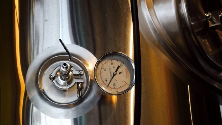 A close-up of a stainless steel brewery tank with a pressure gauge and valve.