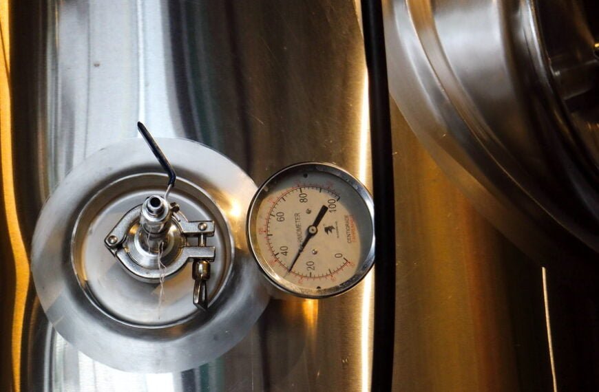 A close-up of a stainless steel brewery tank with a pressure gauge and valve.