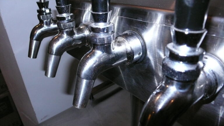 Three metal taps attached to a stainless steel backdrop, with no water flowing.