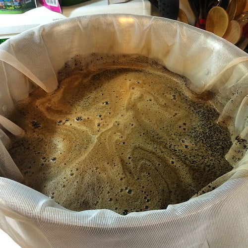 Freshly brewed coffee in a white filter inside a coffee maker, showing bubbles and grounds on the surface.